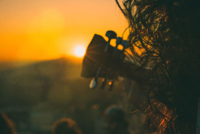 Woman with guitar against sky during sunset