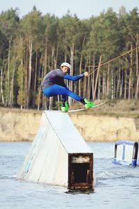 Man performing stunt on wakeboard in lake against trees