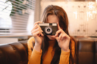 Teenage girl photographing with vintage camera while sitting in cafe