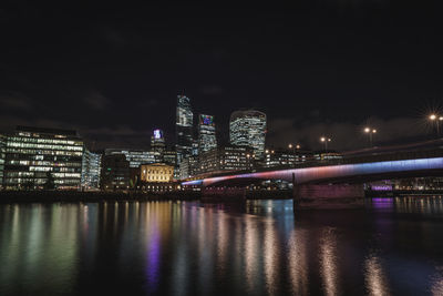 Illuminated buildings by river against sky at night