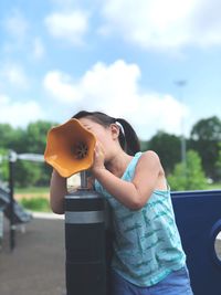 Girl shouting on megaphone at playground against sky