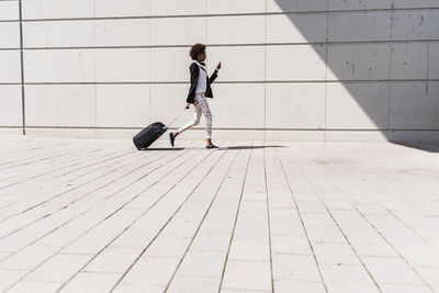 Walking businesswoman with trolley bag looking at her smartphone