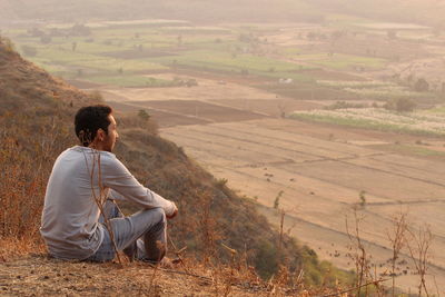 Rear view of man sitting in rural landscape