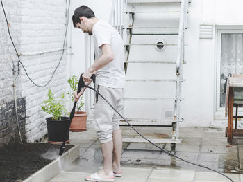 A caucasian guy washes a border of garden tiles enclosing a vegetable garden from a terrace