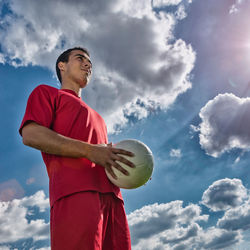 Low angle view of man playing with soccer ball against blue sky during sunny day