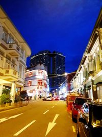 City street by illuminated buildings against sky at night