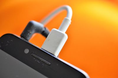 Close-up of mobile phone charging against orange background