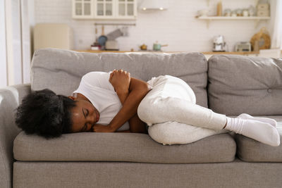 Depressed black girl with crossed arms lying on couch at home crying, suffering from breakup.