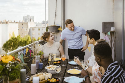 Happy male and female friends talking to each other while celebrating during dinner party in balcony