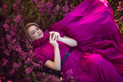 Portrait fashionable beautiful young woman lying in a pink dress in a field with wildflowers 