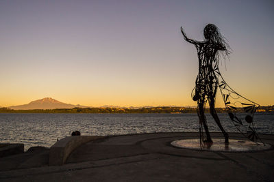 Silhouette statue by sea against clear sky during sunset