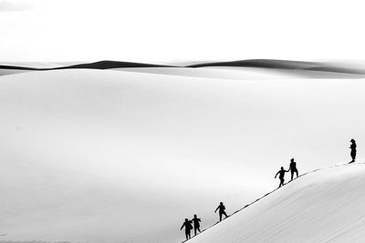 People walking on snow covered land against sky
