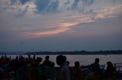 People enjoying at beach against sky during sunset
