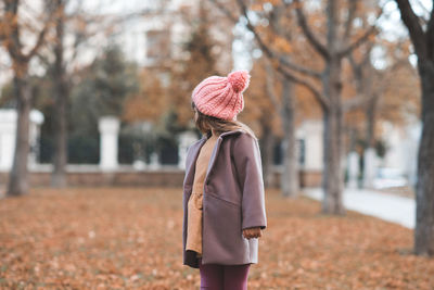 Happy smiling child 4-5 year old wear jacket and hat in park with fall leaves over nature background