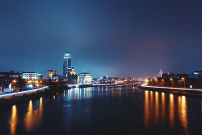 Illuminated buildings by river against sky at night