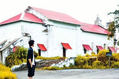 Side view of man standing on road against building