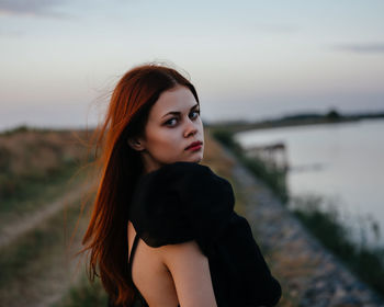 Portrait of young woman standing against sky during sunset