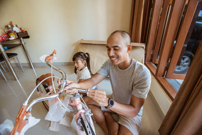 Smiling father assembling bicycle with daughter at home