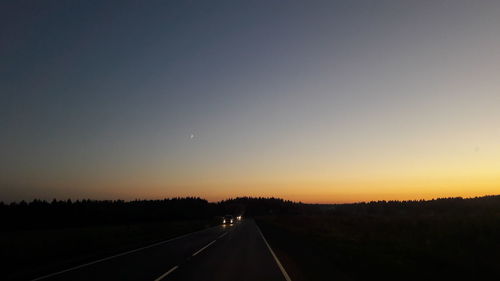 Road amidst silhouette landscape against clear sky during sunset