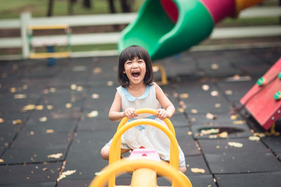 Portrait of smiling girl sitting on seesaw in playground