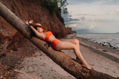 Woman sitting on shore at beach against sky