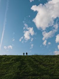 Rear view of people walking on field against sky