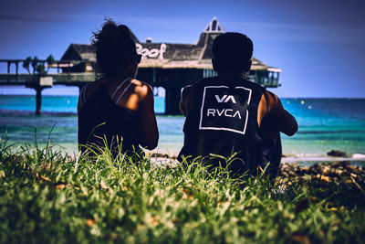 Rear view of men sitting at beach against sky