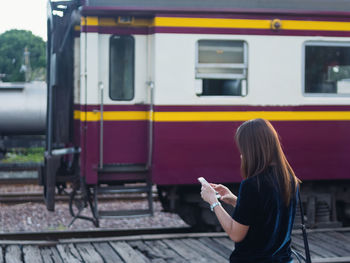 Side view of woman using smart phone while standing against train