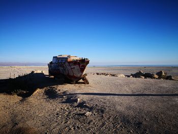 Abandoned boat on beach against clear blue sky