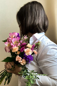 Rear view of woman with pink flowers against wall