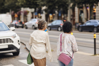 Rear view of disabled woman strolling with female friend at street in city