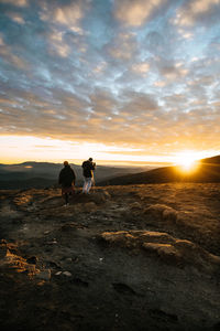 Men standing on land against sky during sunset