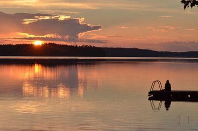 Silhouette men on lake against sky during sunset