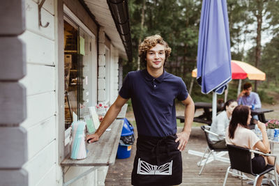 Portrait of young male owner standing outside concession stand while customer sitting in background