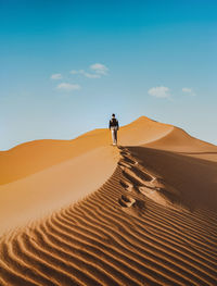 Man on sand dune in desert against sky