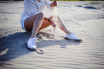 Low section of woman spilling sand at beach