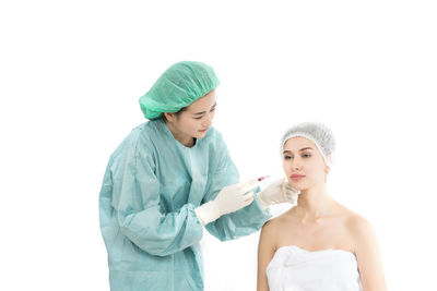 Female doctor injecting examining patient with botulinum toxin injection against white background