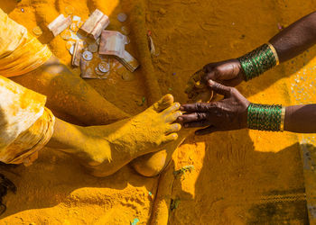 Cropped hand touching turmeric covered feet of man during tradition