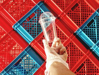 Cropped hand holding disposable cup against crates