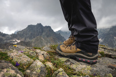Tourist's feet on the rock of the mountain top, in trekking shoes for a hike, close-up
