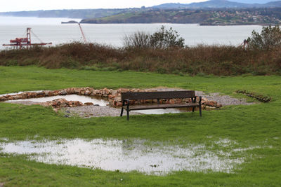 Empty bench on field by lake
