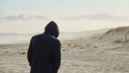 Rear view of man standing on beach against sky