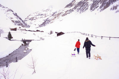 Rear view of people skiing on snowcapped mountain against sky