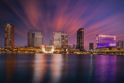 Illuminated city by river against sky at night