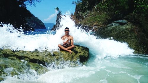 Full length of shirtless man on rock in sea