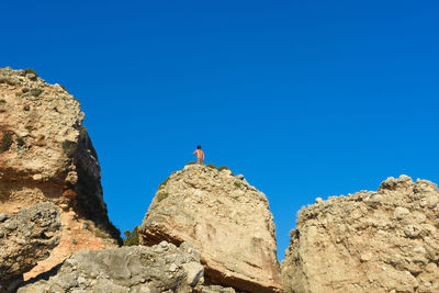 Low angle view of shirtless man on rock formation against clear blue sky
