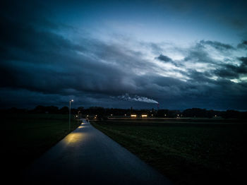Road by illuminated field against sky at dusk