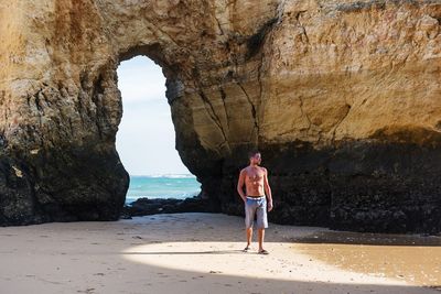 Shirtless young man standing against natural arch on sunny day