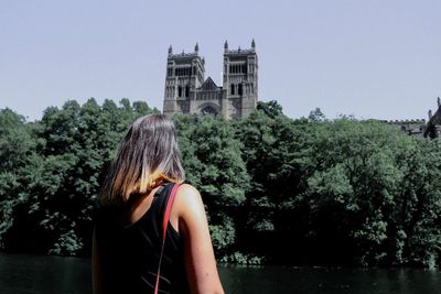 Rear view of woman standing against trees in city