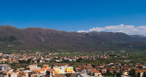 Aerial view of townscape and mountains against blue sky